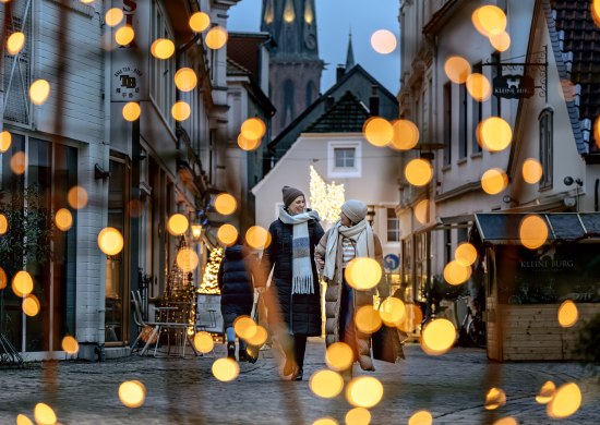 Zwei Frauen gehen durch die weihnachtlich beleuchtete Burgstraße in Oldenburg. 