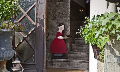 Eine offene T&uuml;r eines Hauseingangs mit einer Figur, die ein Tablett tr&auml;gt.